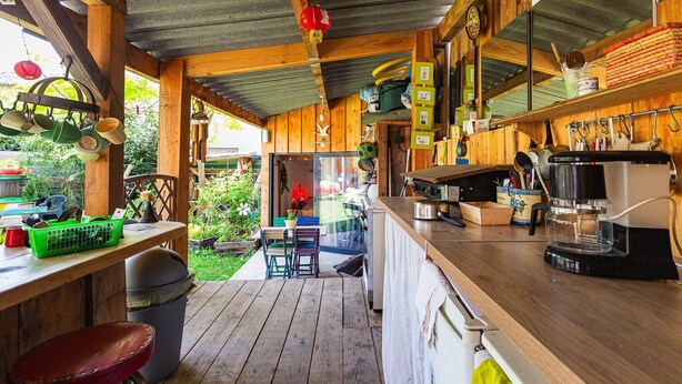 Una cocina de madera con una mesa de madera, sillas, una cafetera y utensilios colgando.