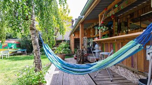 Una terraza de madera con una hamaca, una zona de barbacoa y un bar rústico.