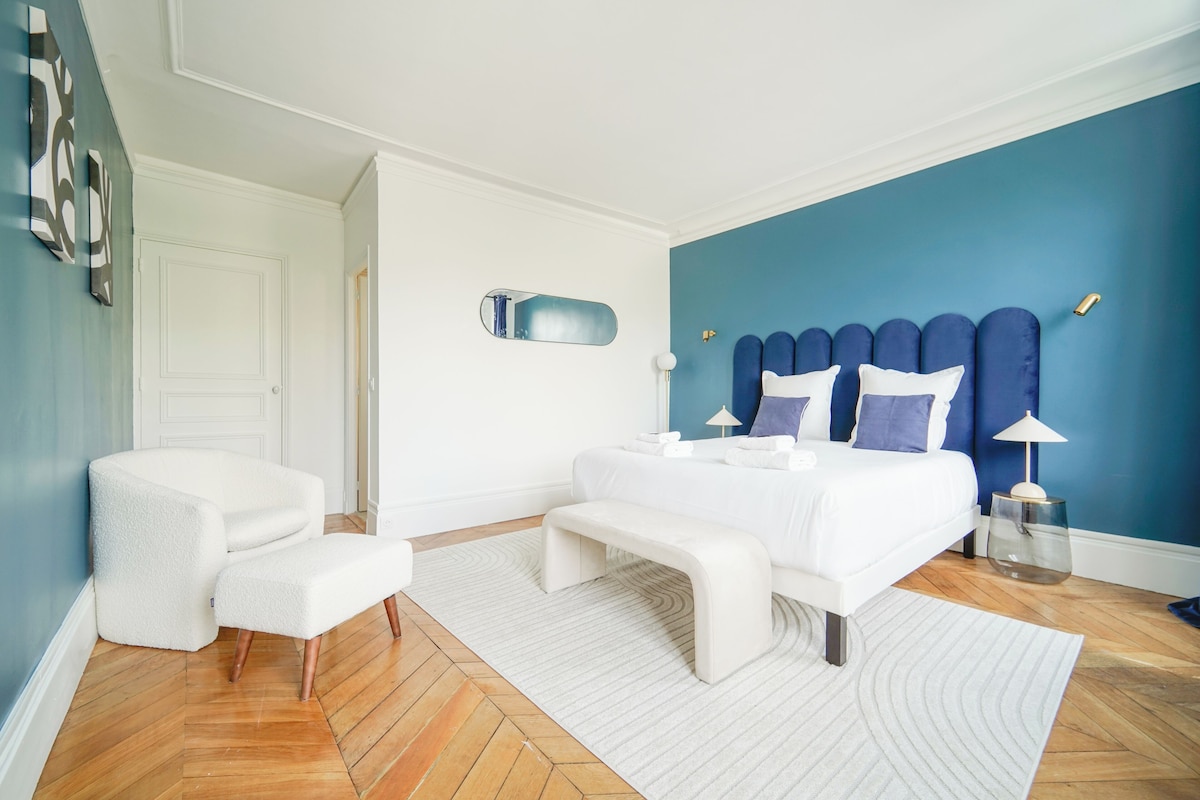 A bedroom with a bed, a bench, a chair, a bedside table, and a lamp.