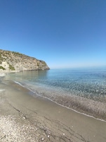 Una playa con agua cristalina, una orilla de arena y un acantilado rocoso.