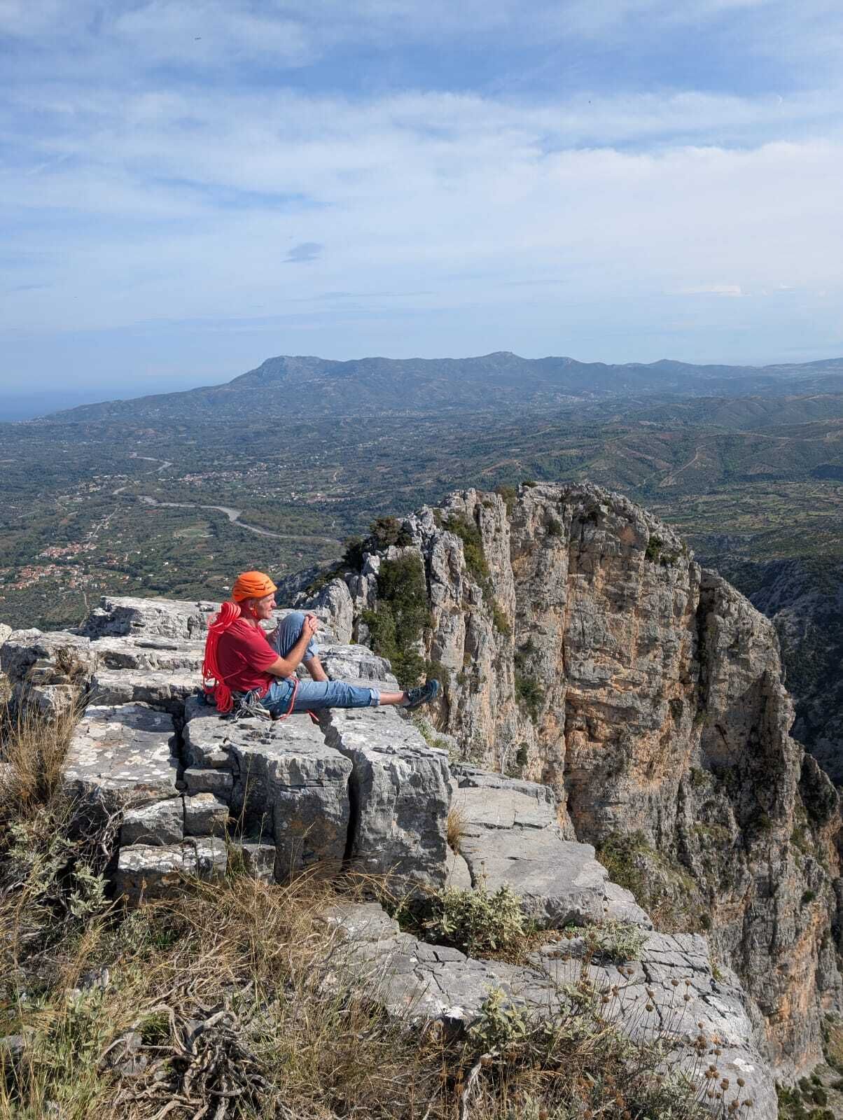Une personne assise sur un rebord rocheux, d’où elle contemple un paysage montagneux.