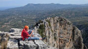 Une personne assise sur un rebord rocheux, d’où elle contemple un paysage montagneux.