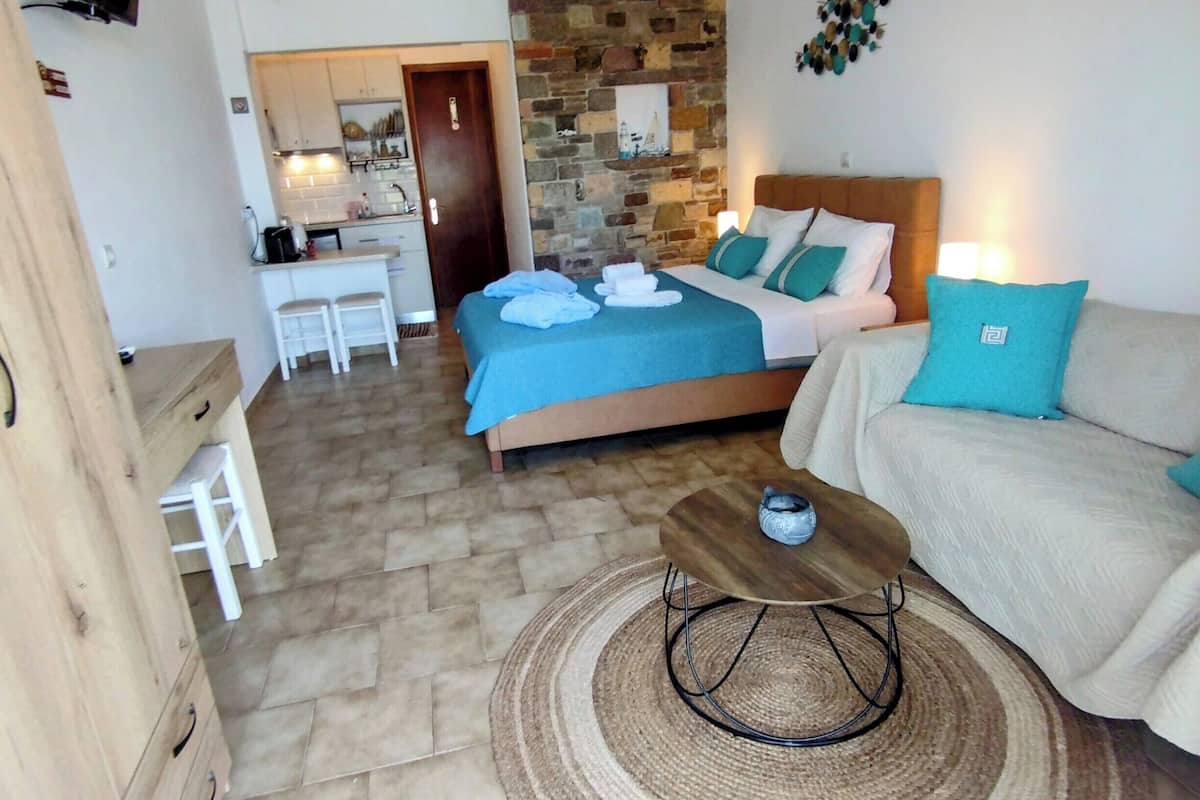 A bedroom with a stone wall, a bed with blue and white bedding, a wooden nightstand, and a sofa with a blue pillow.