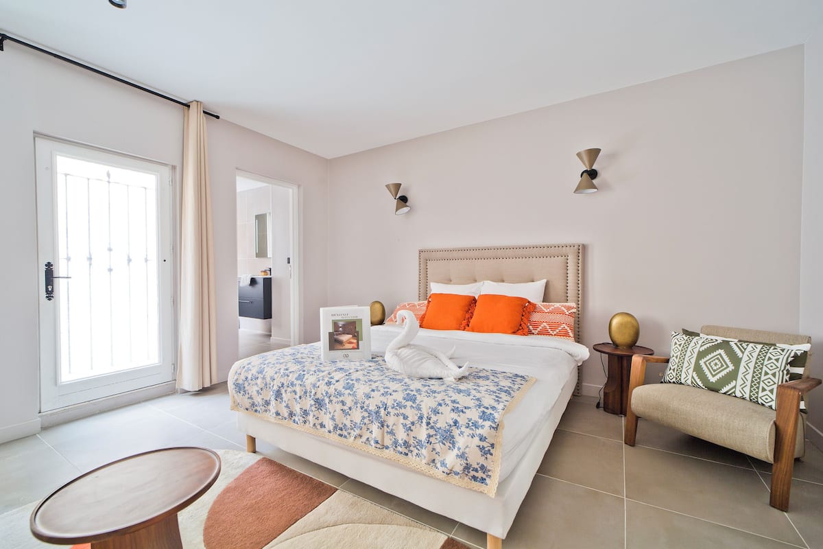 Un dormitorio con cama, mesita de noche, silla y ventana.