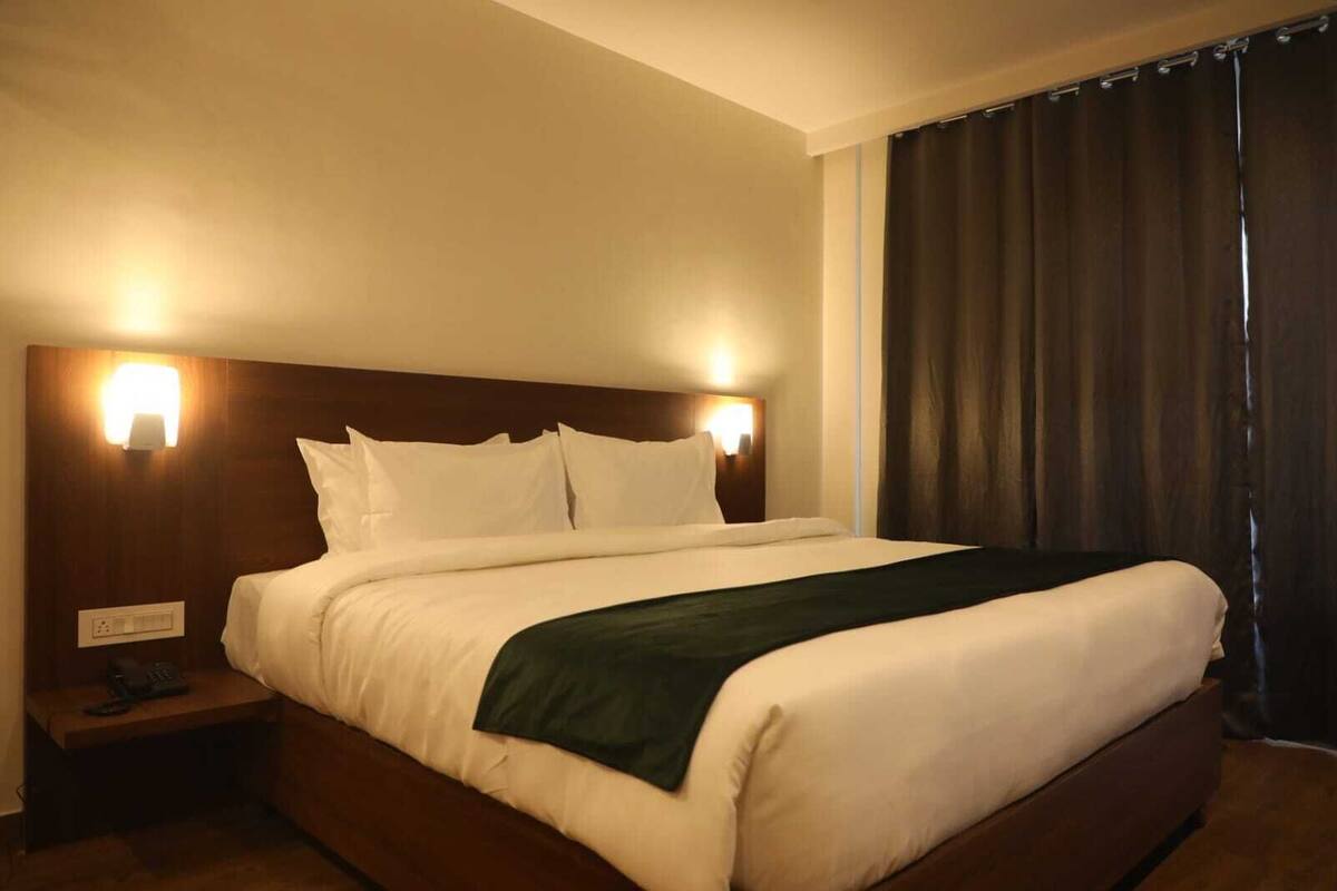 Een hotelkamer met een groot bed, twee bedlampen, een nachtkastje met een telefoon en een raam met donkere gordijnen.