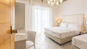 A hotel room with a bed, bedside tables, a chair, a desk, a chandelier, and a window with curtains. - Alda Seaview Hotel (Cervia)