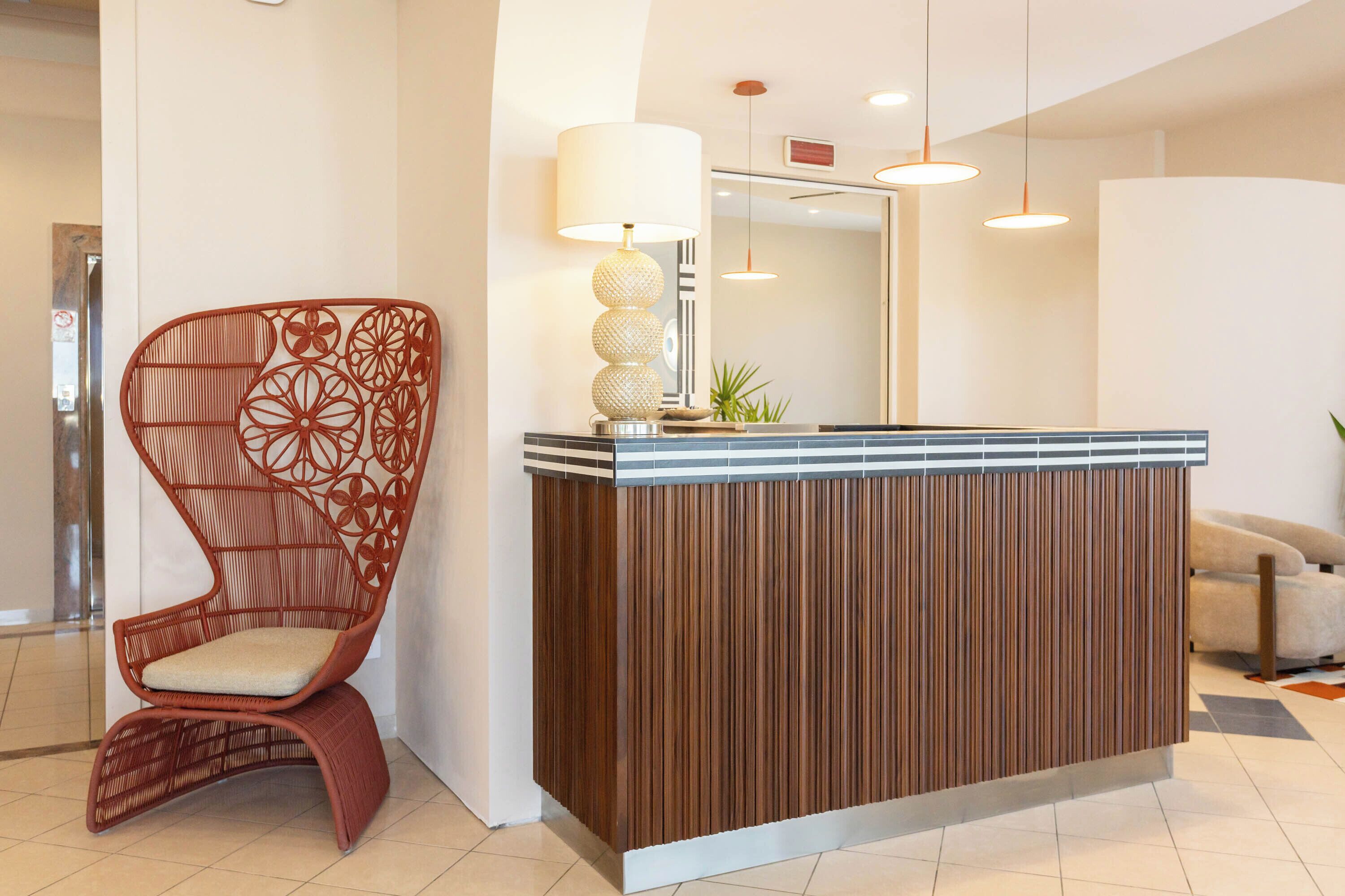 Un mostrador de recepción de diseño moderno, una silla de mimbre con cojín y una lámpara colgante.