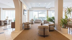 A spacious lobby with a high ceiling, large windows, and a seating area with sofas and armchairs. - Alda Seaview Hotel (Cervia)