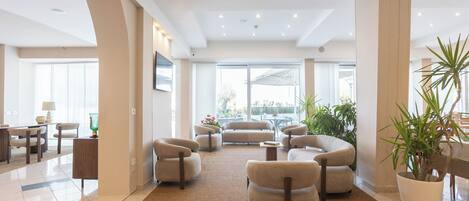 A spacious lobby with a high ceiling, large windows, and a seating area with sofas and armchairs.