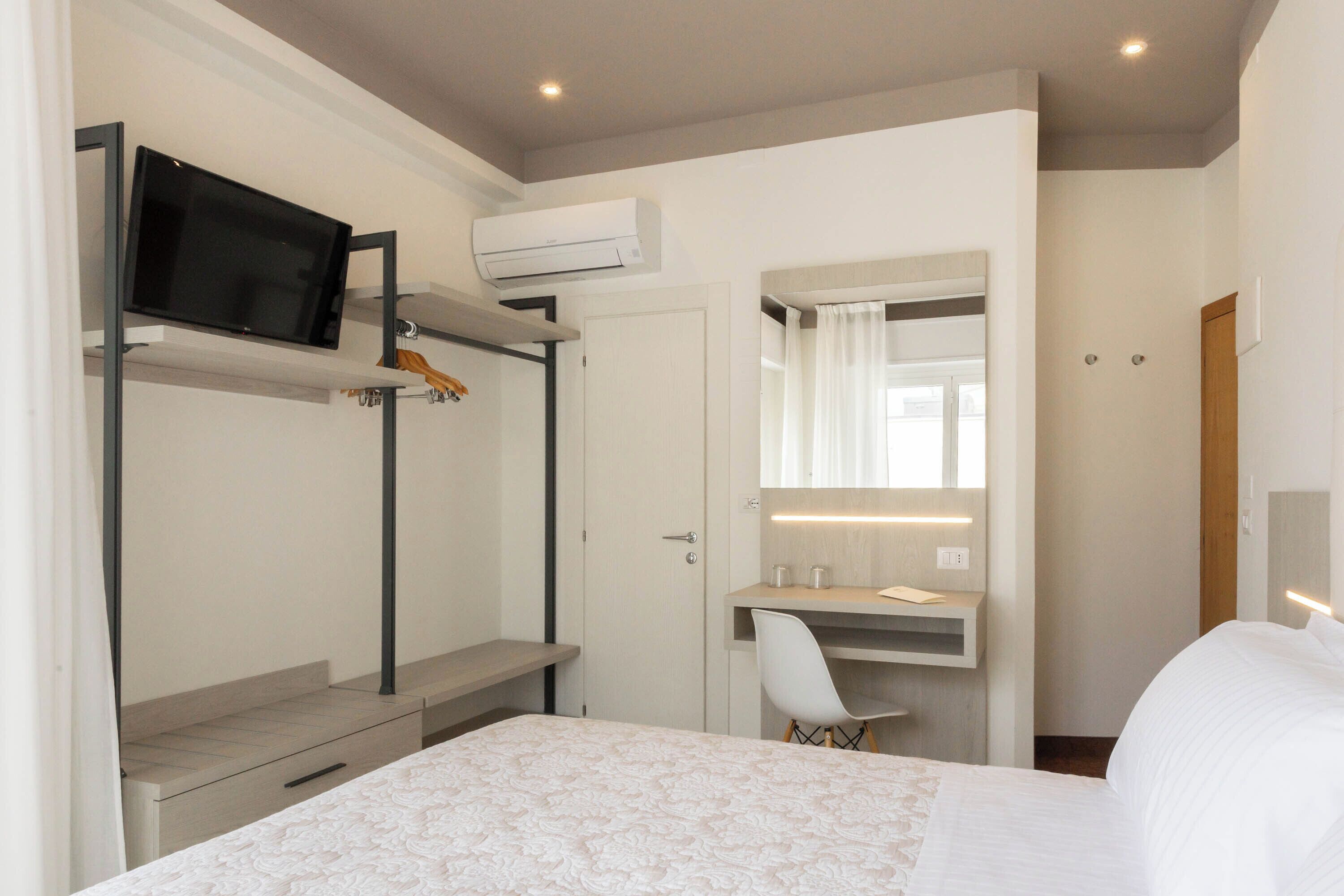 Habitación de hotel con cama, escritorio con silla, televisor montado en una repisa y espejo sobre el escritorio.