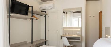 Habitación de hotel con cama, escritorio con silla, televisor montado en una repisa y espejo sobre el escritorio.
