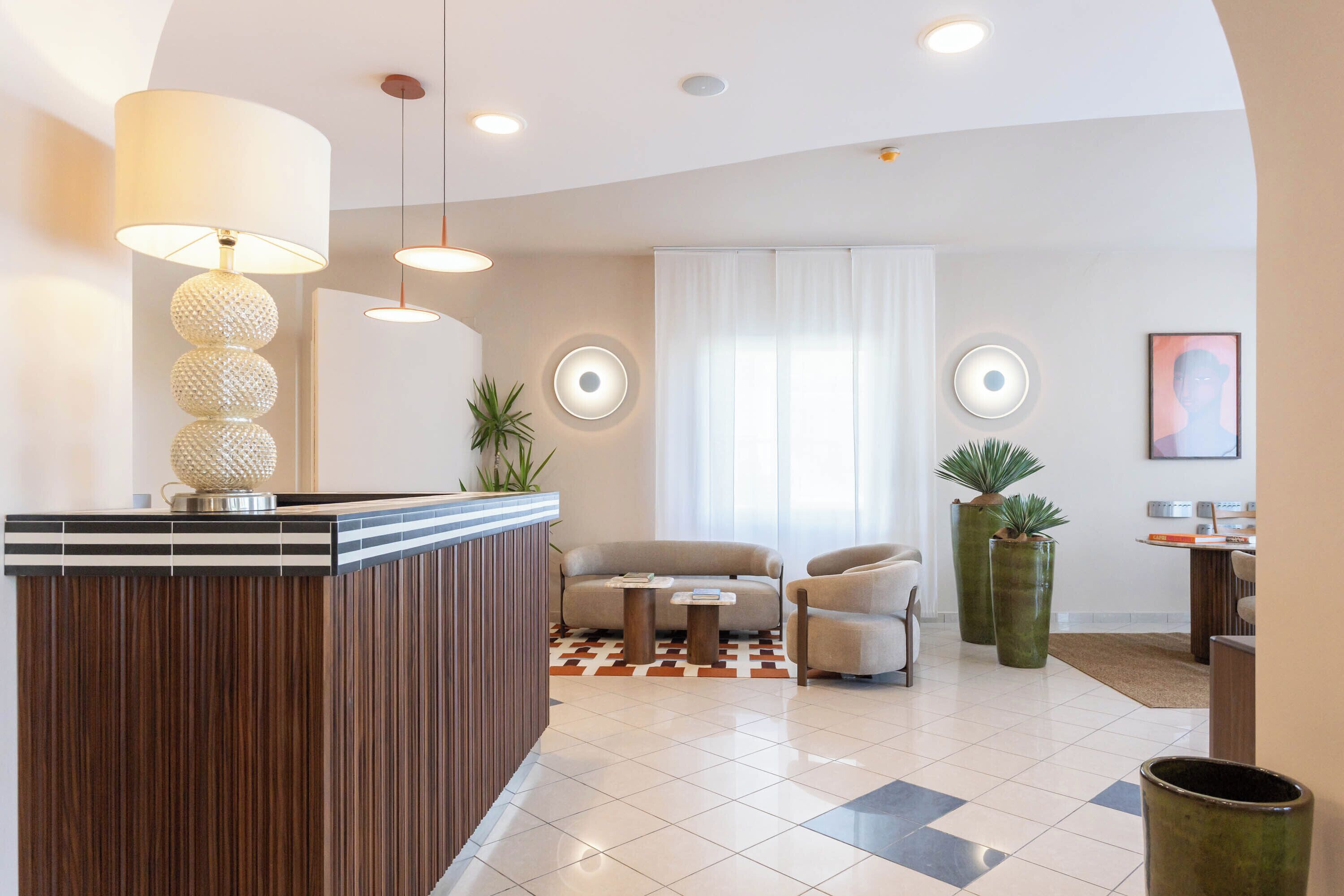 A modern hotel lobby with a reception desk, seating area, and large potted plants.
