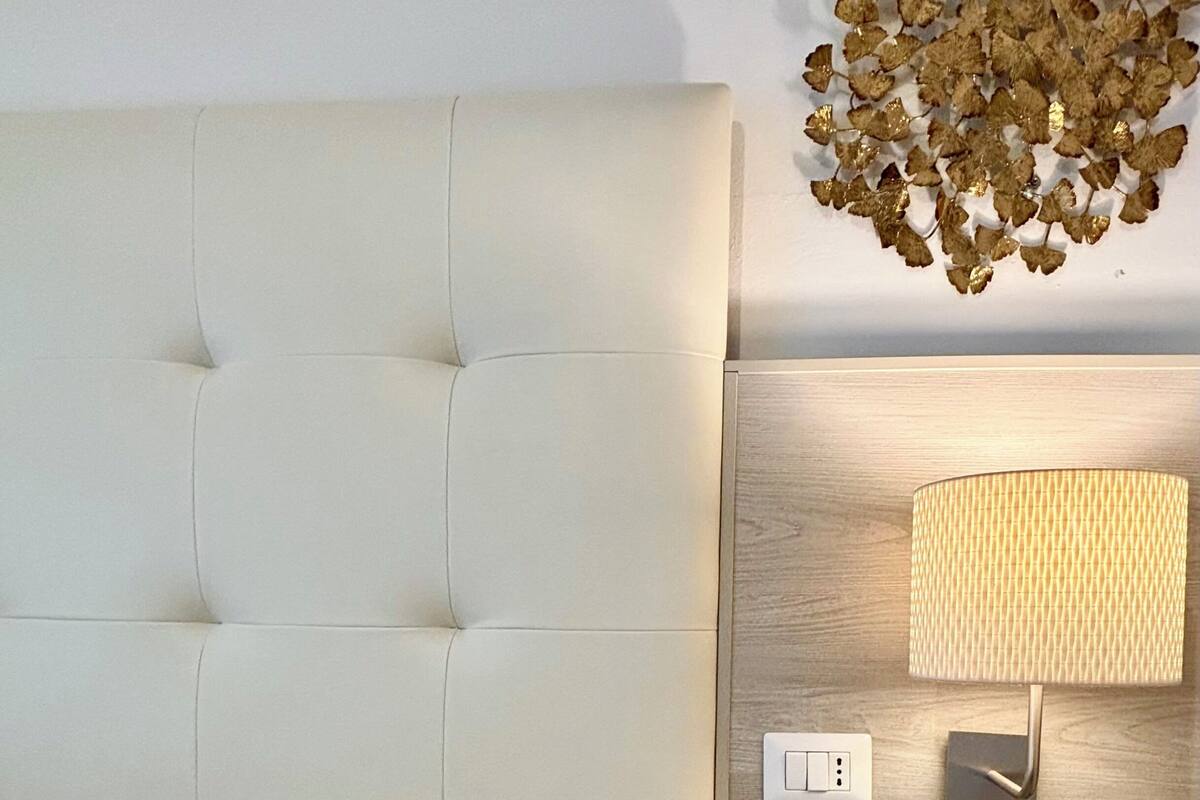 Un dormitorio con cabecera capitonada, una mesita de noche con lámpara y un adorno de pared.