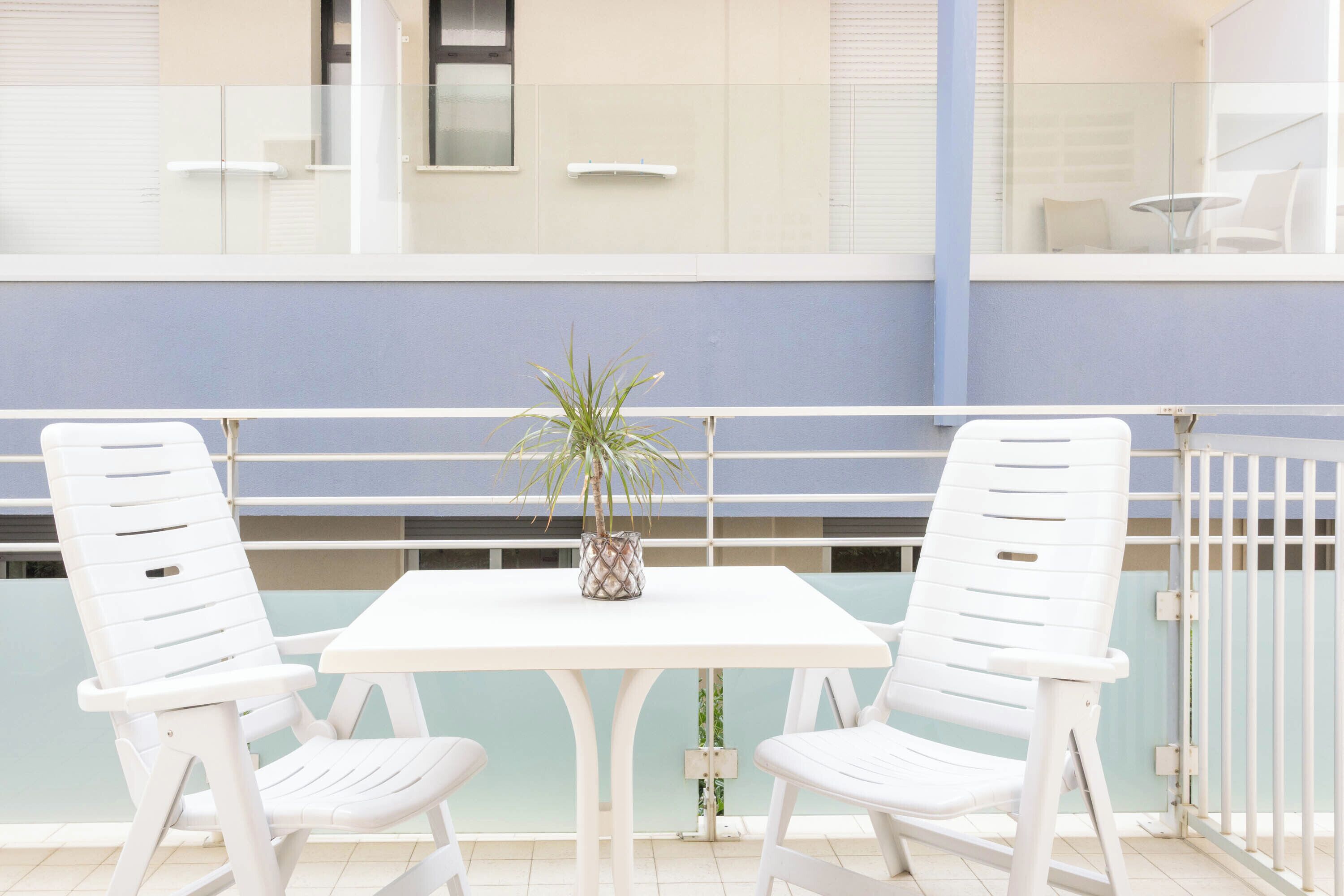 A balcony with two white chairs, a small table, and a potted plant.