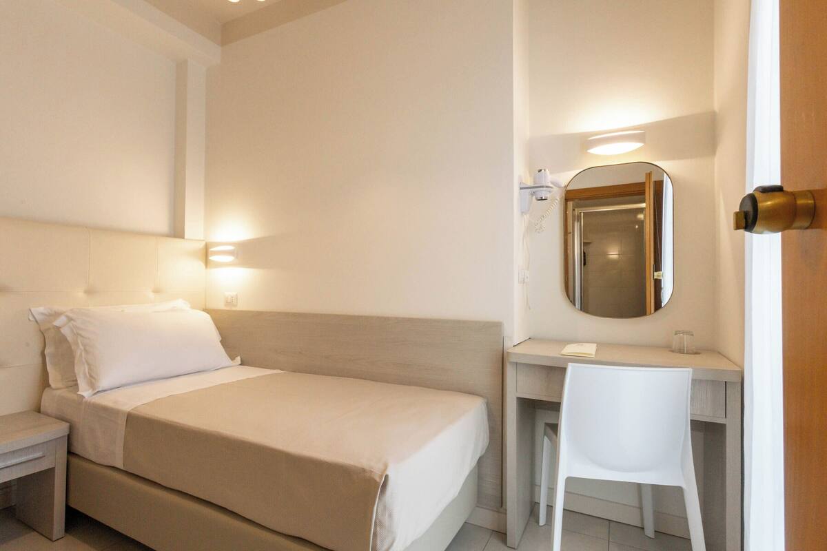 Un dormitorio con cama, mesita de noche, escritorio, silla y espejo.