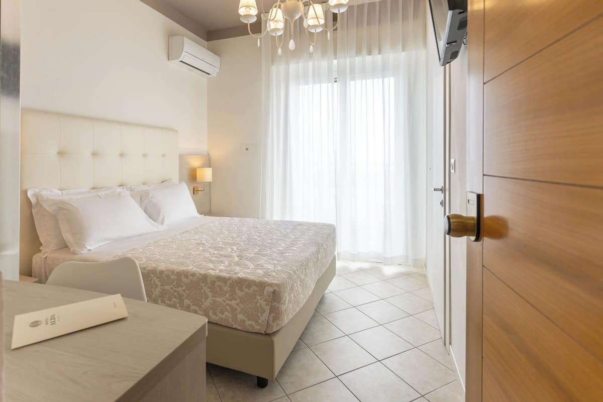Una habitación de hotel con cama, mesita de noche y armario de madera.