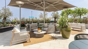 An outdoor seating area with a large umbrella, wicker furniture, a round table, and potted plants. - Alda Seaview Hotel (Cervia)