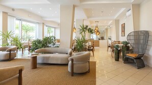 A spacious lobby with a sofa, chairs, a dining area, and potted plants. - Alda Seaview Hotel (Cervia)
