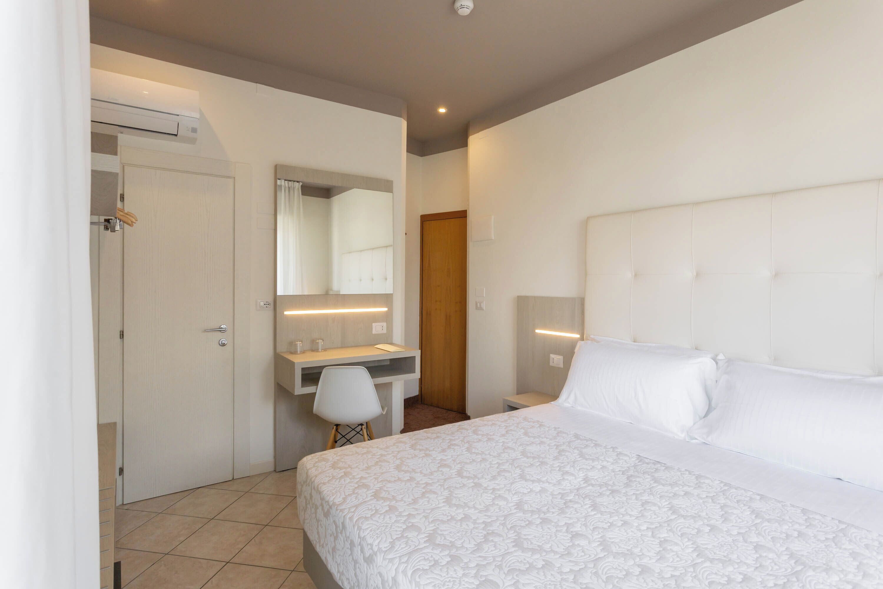 A bedroom with a bed, a desk, a chair, a mirror, and a door.