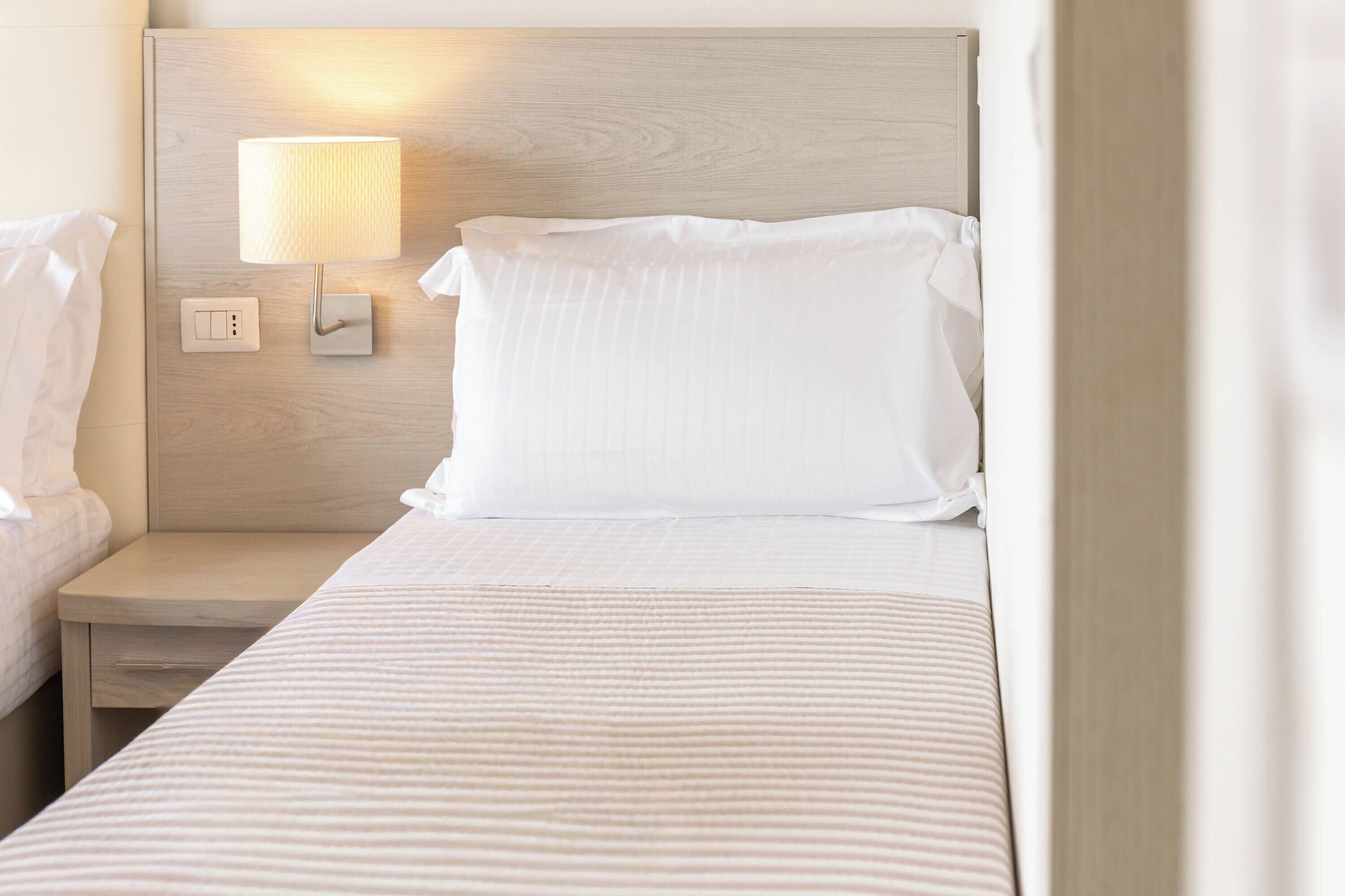 A hotel room with a bed, a bedside table, a lamp, and a wall-mounted light.