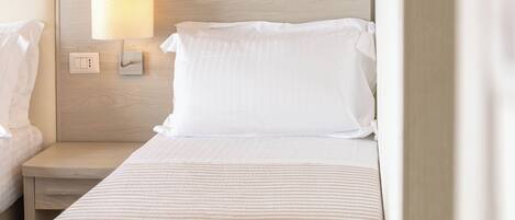 A hotel room with a bed, a bedside table, a lamp, and a wall-mounted light.