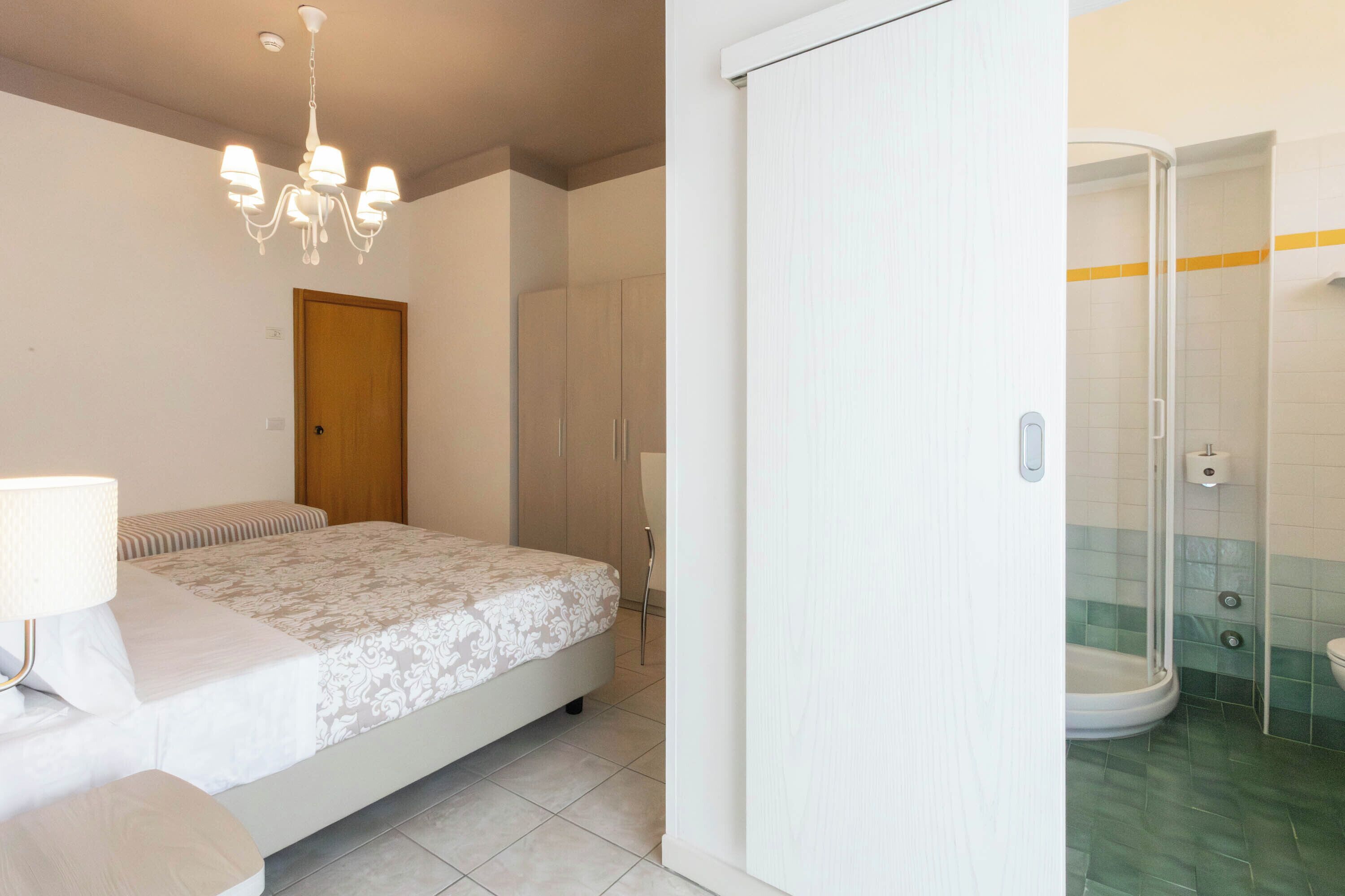 A bedroom with a bed, bedside table, and a chandelier.