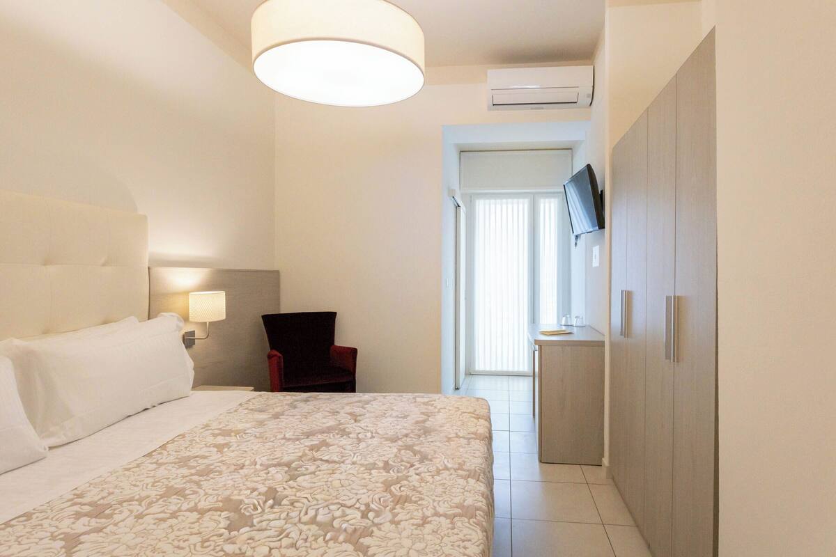 Una habitación de hotel con una cama grande, un escritorio con silla, un televisor y un armario.