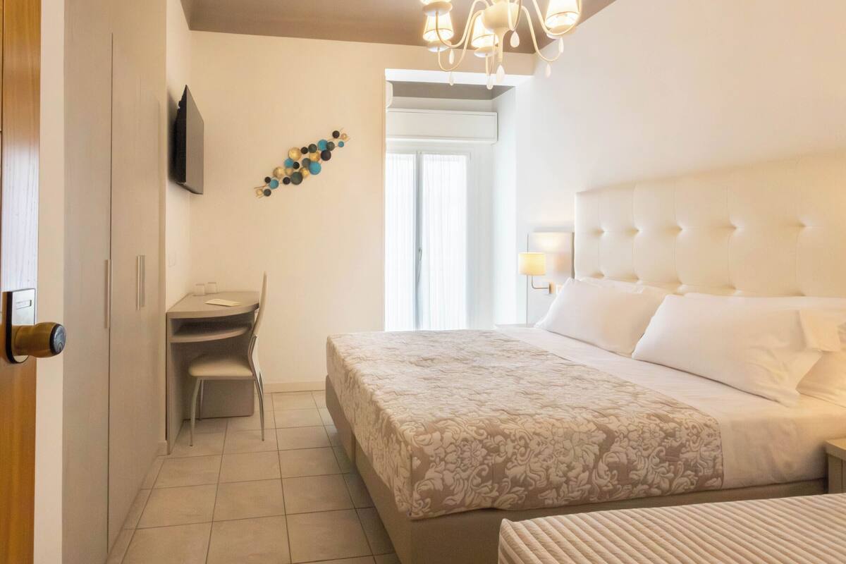 Una habitación de hotel con cama, escritorio, silla, televisión y candelabro.