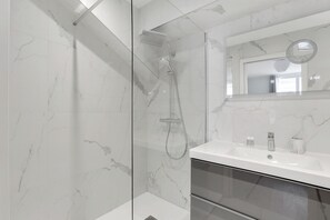 A modern bathroom with a glass-enclosed shower, a white sink, and a mirror above it. - Appartements Boulevard Pereire (Paris)