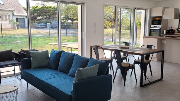 Un soggiorno moderno con un divano blu, un tavolo da pranzo con sedie e un angolo cottura con fornelli e microonde.