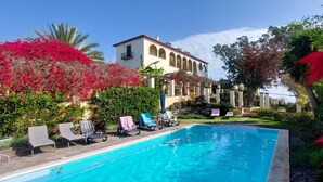 A swimming pool with lounge chairs, surrounded by lush greenery and a building with arched windows. - Cozy Studio in a fabulous Quinta with pool and sea view! (Funchal)