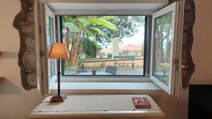 A room with a desk and a window. The window has a view of a garden with trees and a bench. - Cozy Studio in a fabulous Quinta with pool and sea view! (Funchal)