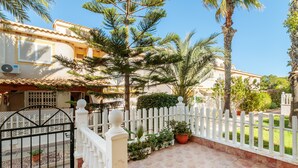 Un patio con valla blanca, plantas en macetas y una palmera.