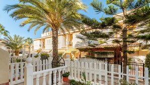 Un patio con cerca blanca, palmeras y un edificio con balcones.