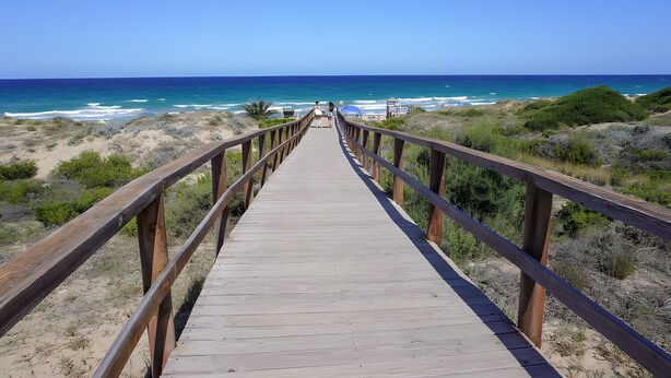 Un muelle de madera que conduce a una playa con cielos despejados.