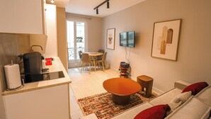 A modern living room with a sofa, a coffee table, and a dining area with chairs and a table. - Appartements rue Amélie (Paris)