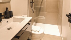 A modern bathroom with a glass-enclosed shower, a white sink, and a toilet. - Appartements rue Amélie (Paris)