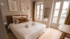 A neatly made bed with two towels, a wooden headboard, and a small bedside table. - Appartements rue Amélie (Paris)