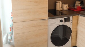 A compact kitchen with wooden cabinets, a microwave, a coffee maker, a toaster, and a washing machine. - Appartements rue Amélie (Paris)
