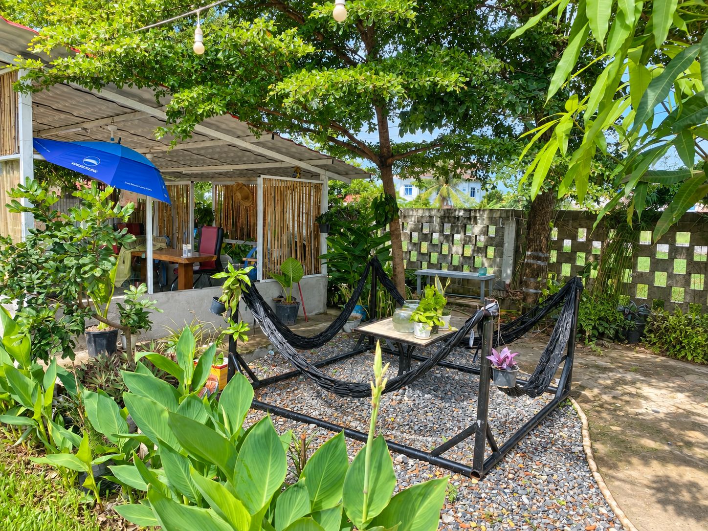 A covered outdoor seating area with a table and chairs, surrounded by potted plants and a hammock.