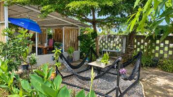 A covered outdoor seating area with a table and chairs, surrounded by potted plants and a hammock.