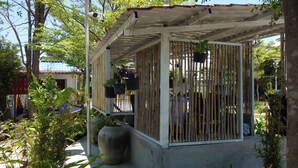 Uma área externa coberta com cercas de bambu, plantas em vasos e piso de concreto.
