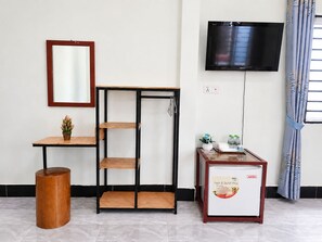 A room with a wooden table, a metal shelf unit, a television, and a small refrigerator. - AHHA Bungalow Kampot (Kampot)