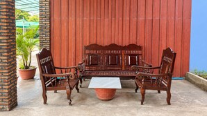 Un patio con mesa y sillas de madera, plantas en macetas y un muro de madera rojo.