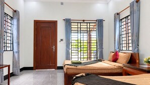Habitación de hotel con dos camas, una puerta de madera y vistas a través de una ventana con barrotes.