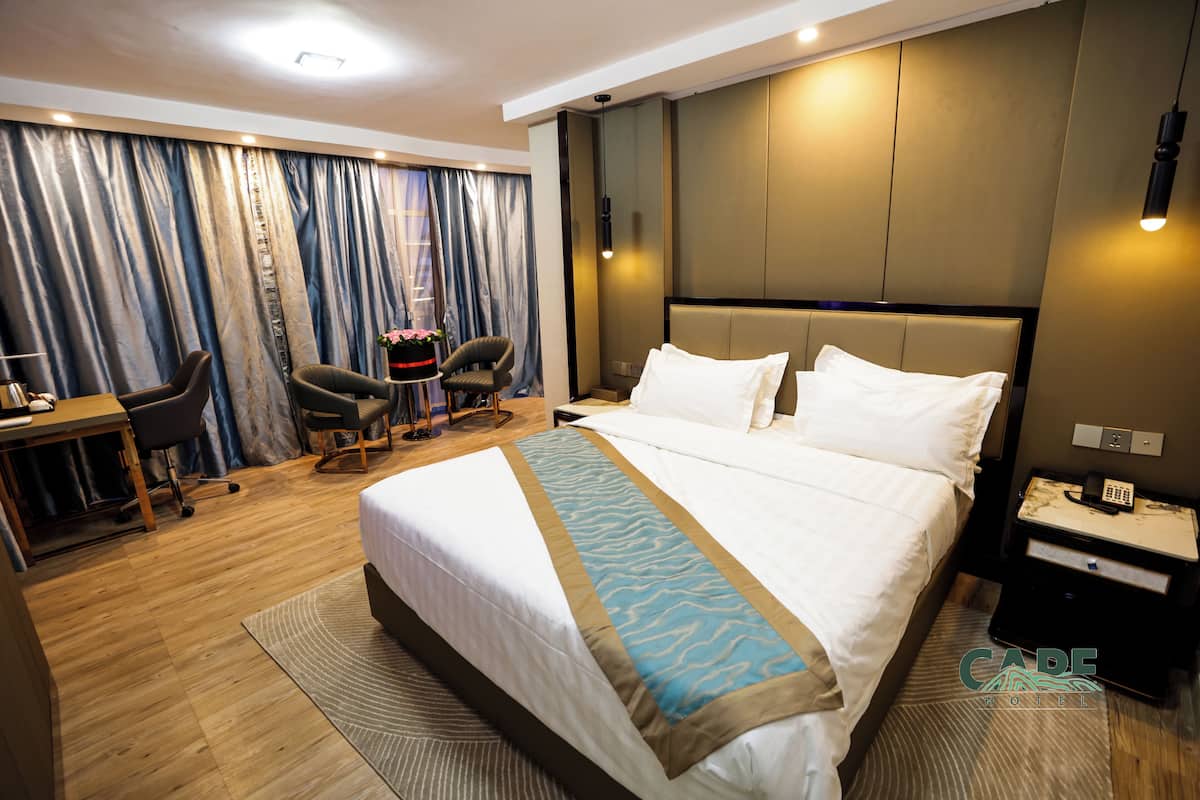 Een hotelkamer met een groot bed, een bureau met stoel, een klein tafeltje met vaas en een nachtkastje met telefoon.