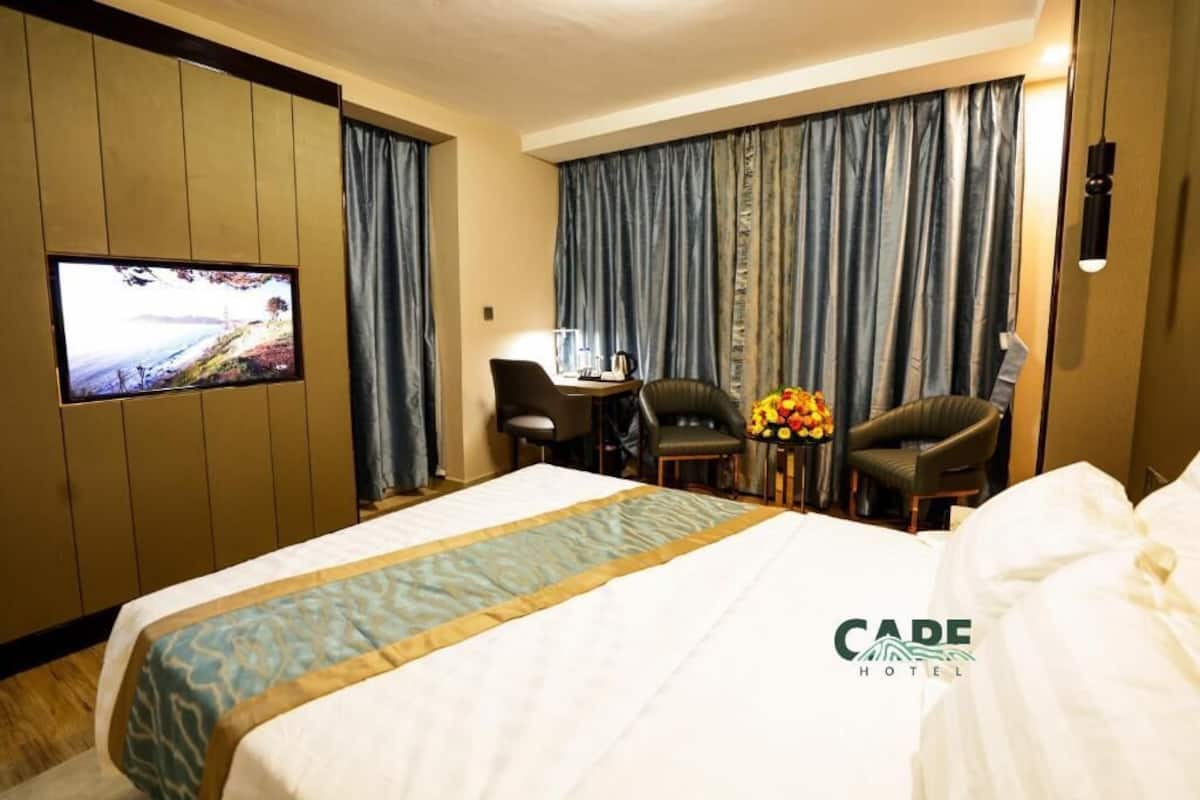 Een hotelkamer met een bed, een bureau, twee stoelen, een televisie en een televisie aan de muur.