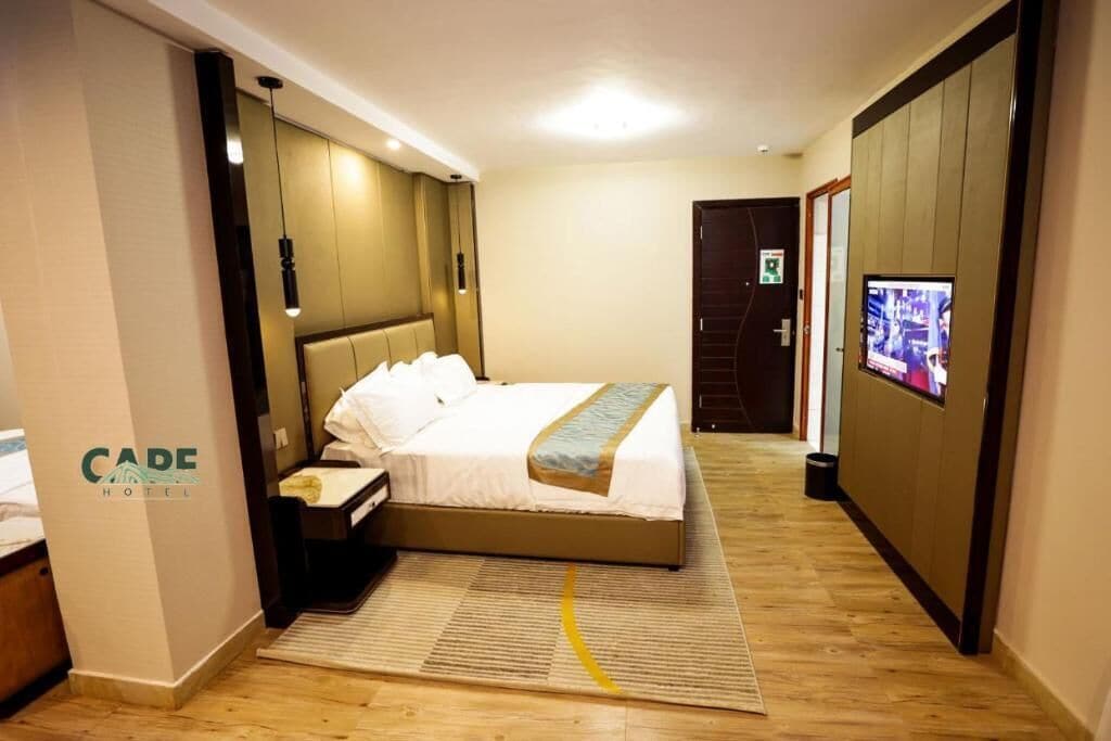 Una habitación de hotel con cama, mesita de noche, lámpara y televisión en la pared.