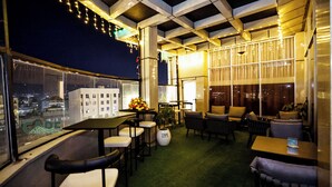 A rooftop bar with tables and chairs, a green carpet, and a view of the city at night. - Cape Hotel (Addis Ababa)