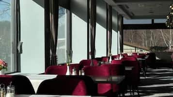 A restaurant with tables and chairs, large windows, and a modern ceiling design.